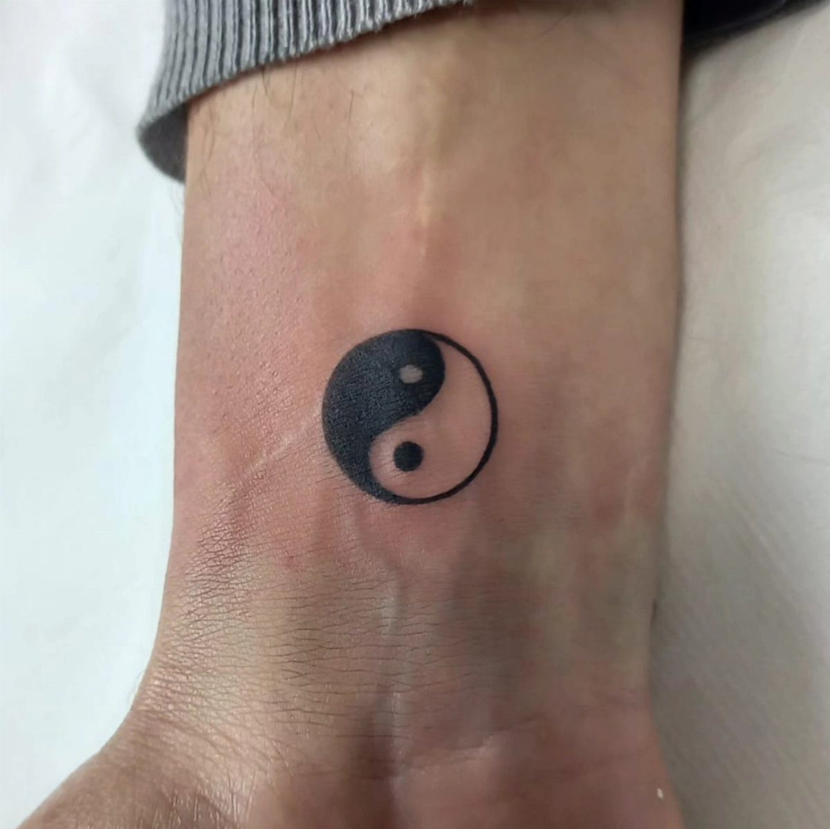 Yin yang symbol tattoo in black and white on a person's ankle.